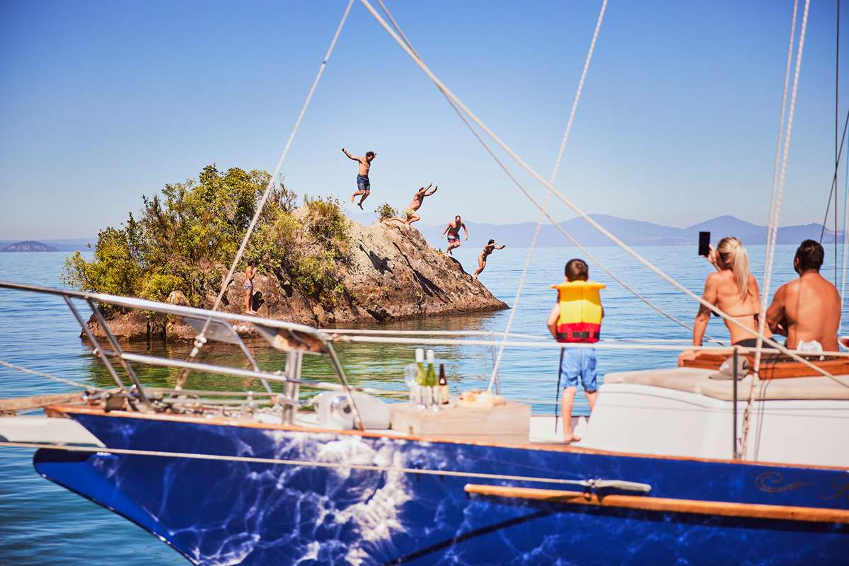 Group of friends jumping off rock into Lake Taupo - sailing cruise - Mine Bay, New Zealand